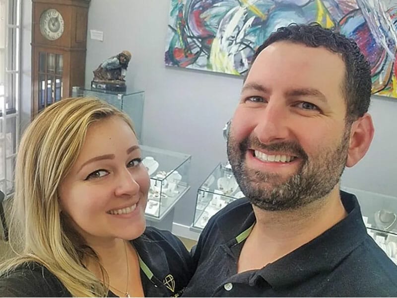 A man and woman smiling in front of a display of jewelry.