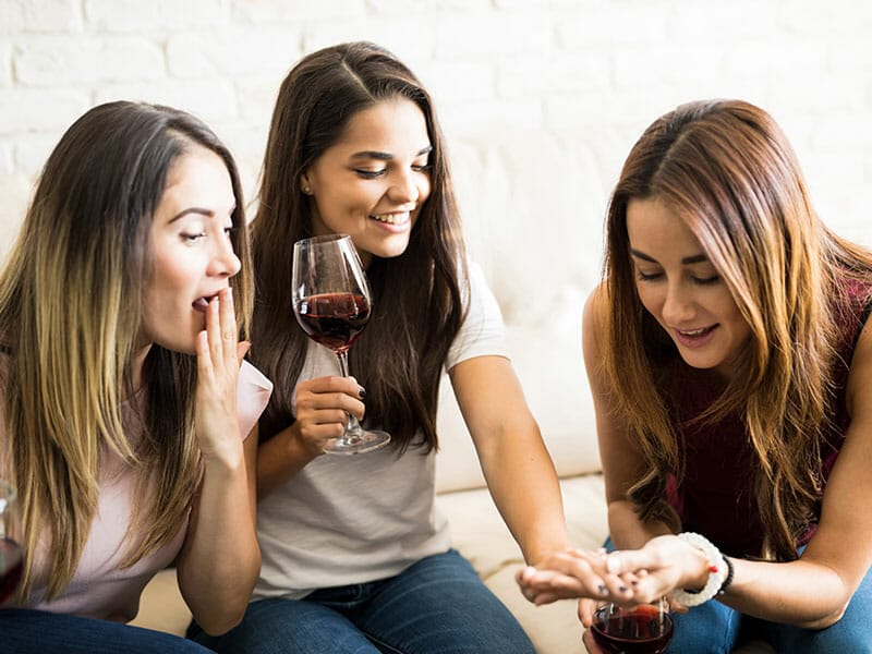 Three women sitting on a couch with glasses of wine.