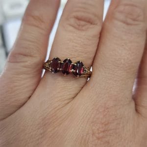 A woman's hand holding a ring with three garnet stones.
