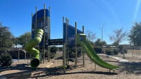 A playground with a green slide and green grass.