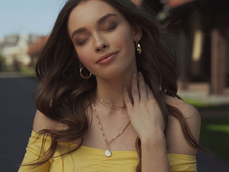 A young woman wearing a yellow dress and necklace with earrings.