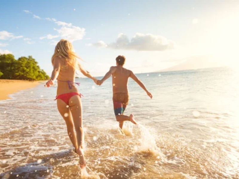 Two people running in the water on a beach.