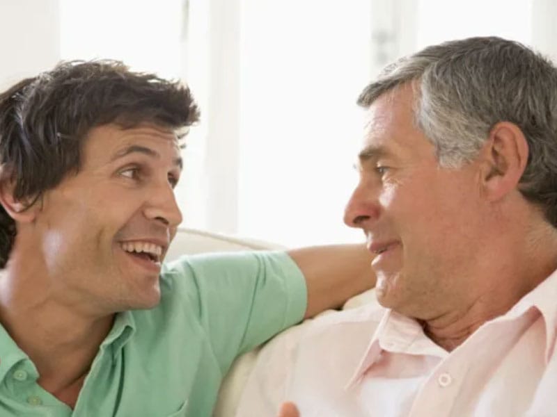 Two men sitting on a couch talking to each other.