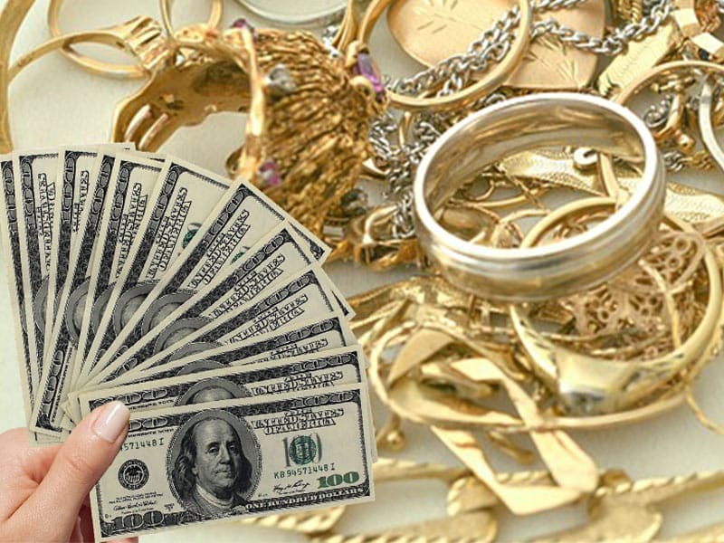 A hand holding money and a stack of gold jewelry.