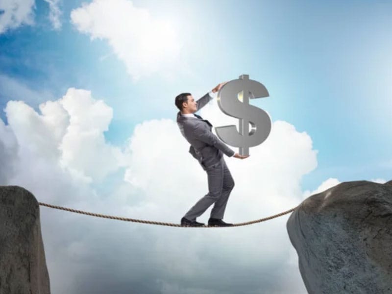 A businessman balancing on a rope holding a dollar sign.