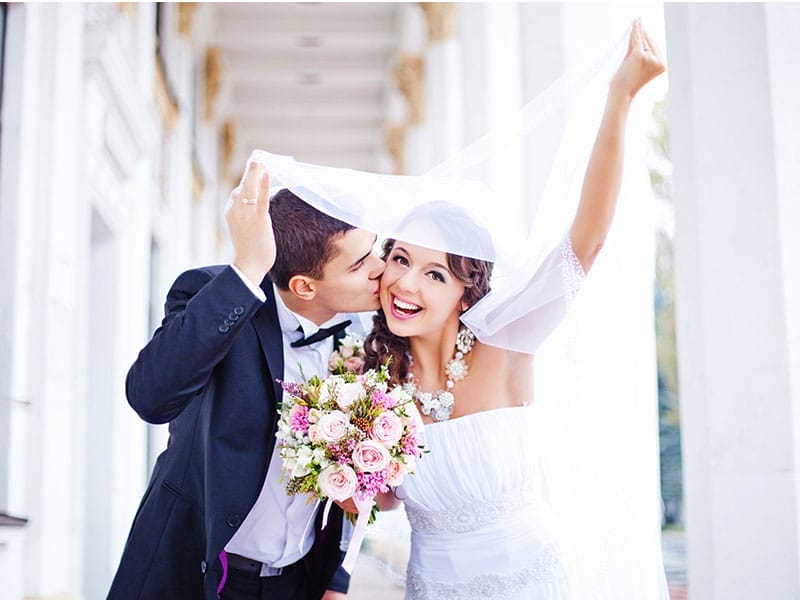 A bride and groom kissing in front of a building.