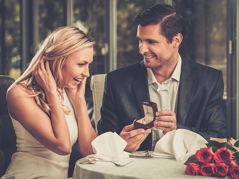 A man and woman sitting at a table with an engagement ring.
