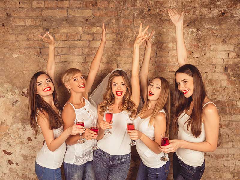 A group of women holding wine glasses in front of a brick wall at a Bachelorette Party.