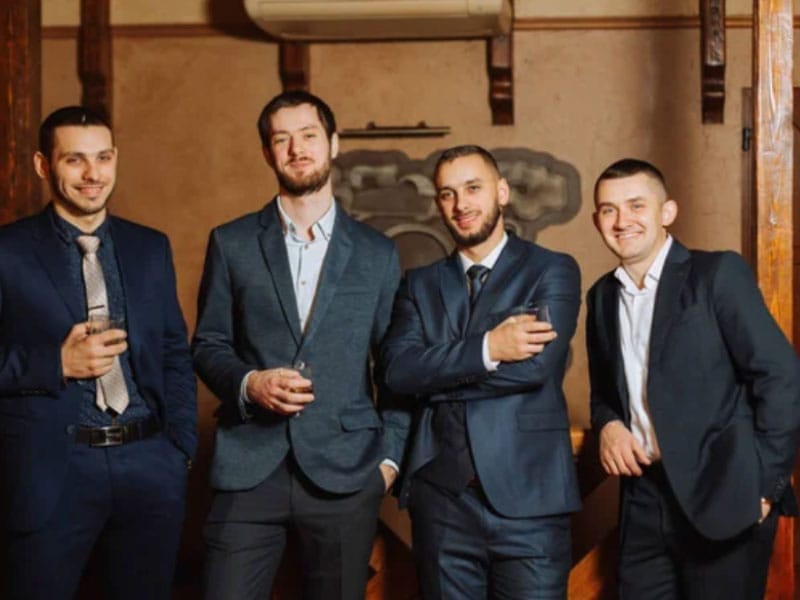 A group of men in suits at a Bachelor Party posing for a picture.