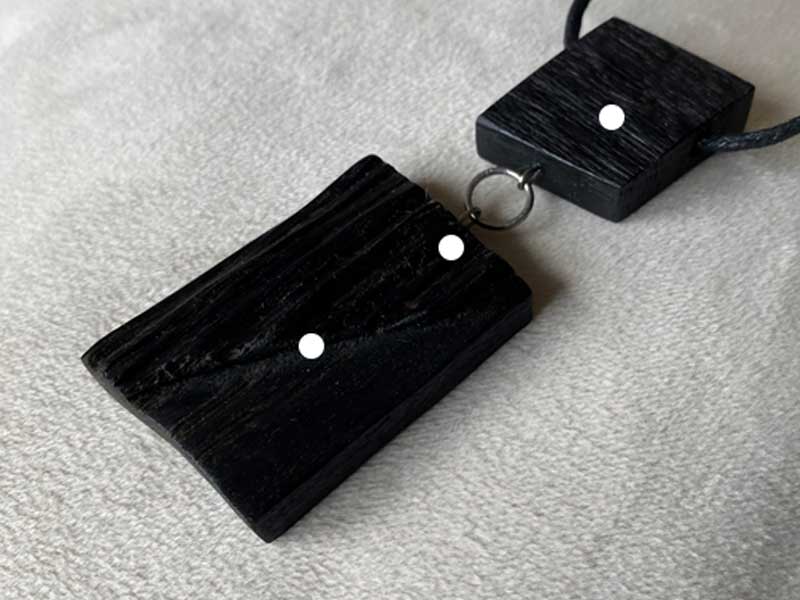 Two black bog oak pendants with white dot detailing on a light grey textile surface.