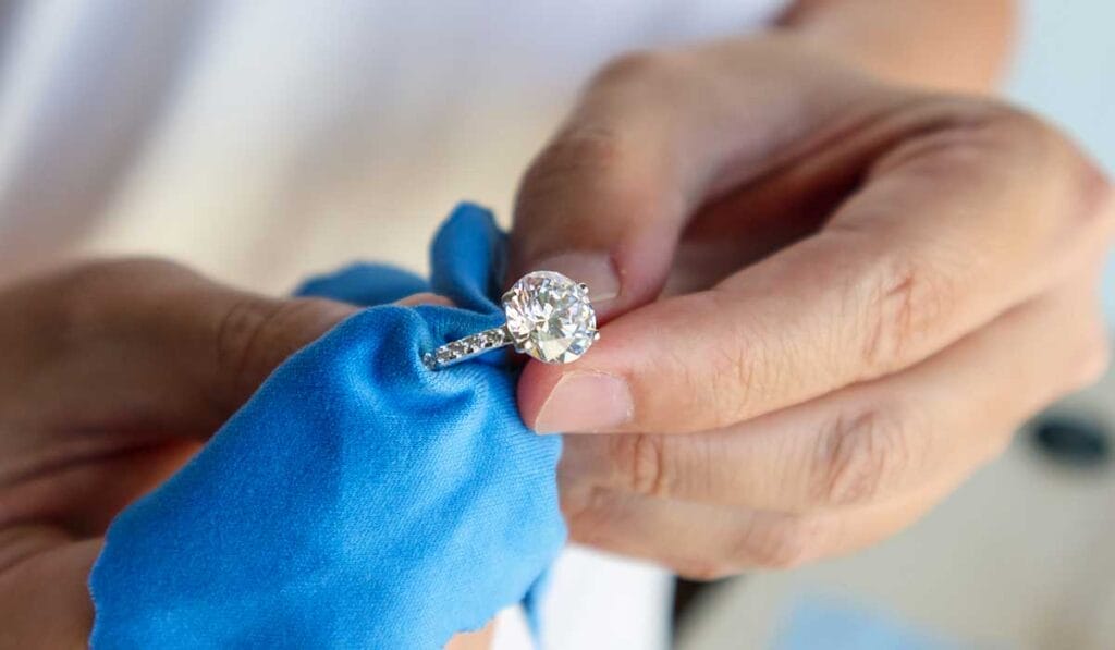 A person is polishing a Princess Cut diamond ring with a blue cloth.