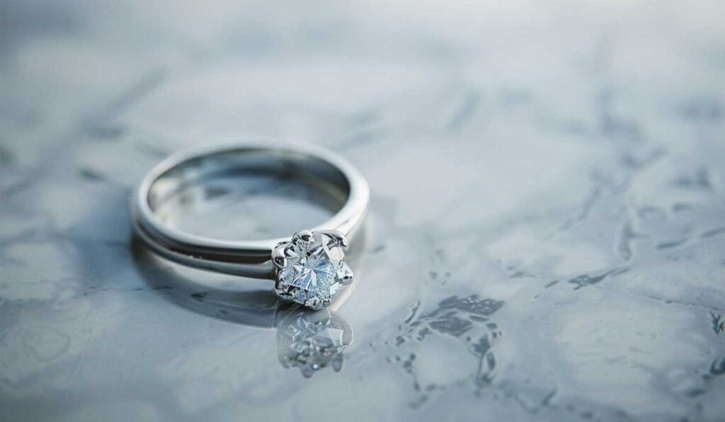 Close-up of a silver ring with a diamond on a textured, reflective surface.