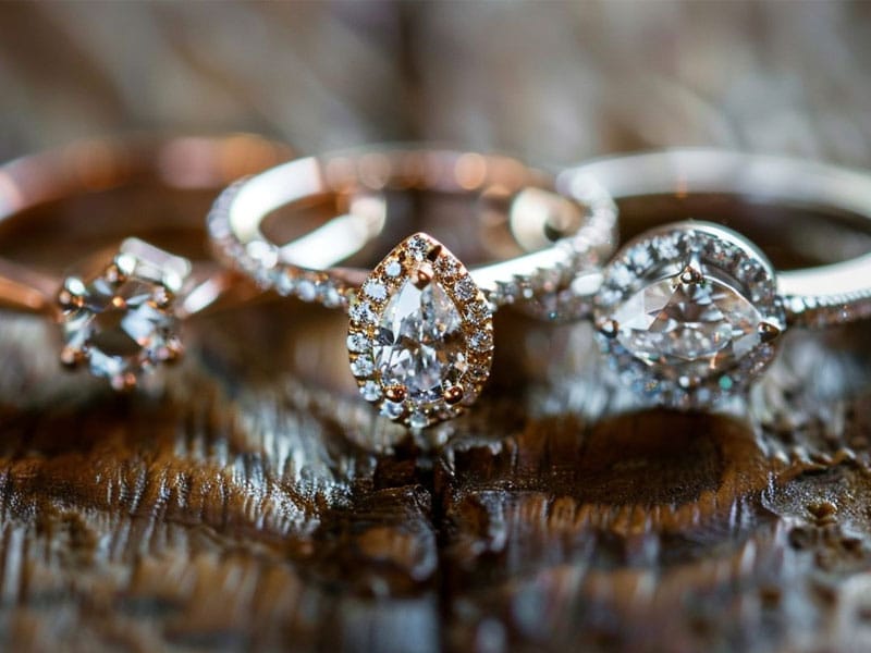 Three diamond engagement rings with different cuts rest on a wooden surface.