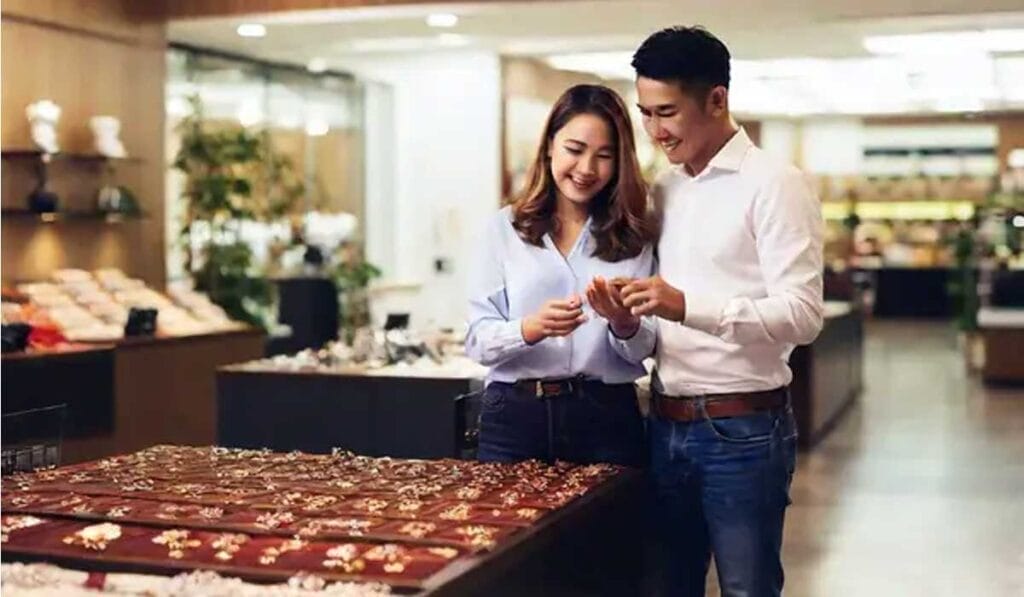 A couple is browsing jewelry in a store, smiling and examining items from a display case filled with rings and other pieces.