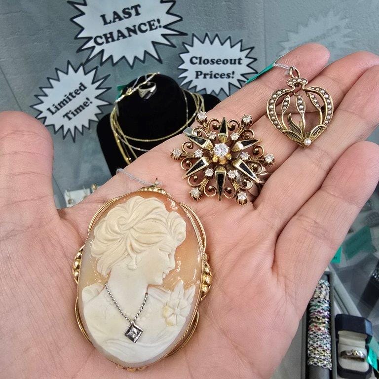 Hand holding a cameo brooch, a sunburst pendant, and a heart-shaped pendant, with a jewelry display and signs indicating "Last Chance!", "Limited Time!", and "Closeout Prices!" in the background.