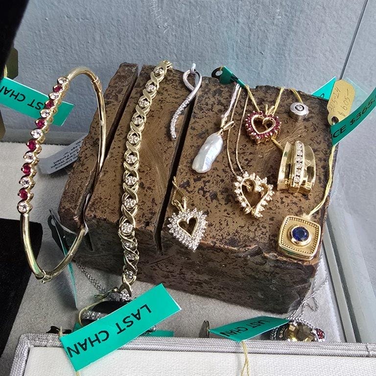 Assorted jewelry pieces including gold necklaces, bracelets, and rings with heart pendants and gemstones, placed on a wooden display block, some tagged with "LAST CHANCE.