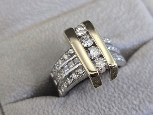 A gold and silver ring with three rows of embedded diamonds on a gray fabric background.